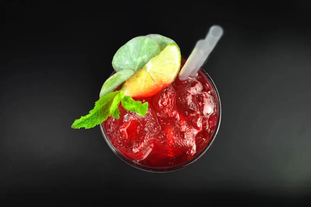 آبمیوه قرمزی که در لیوان ریخته شده است و لیمو و برگ سبزیجات نیز در بالای لیوان قرار گرفته است