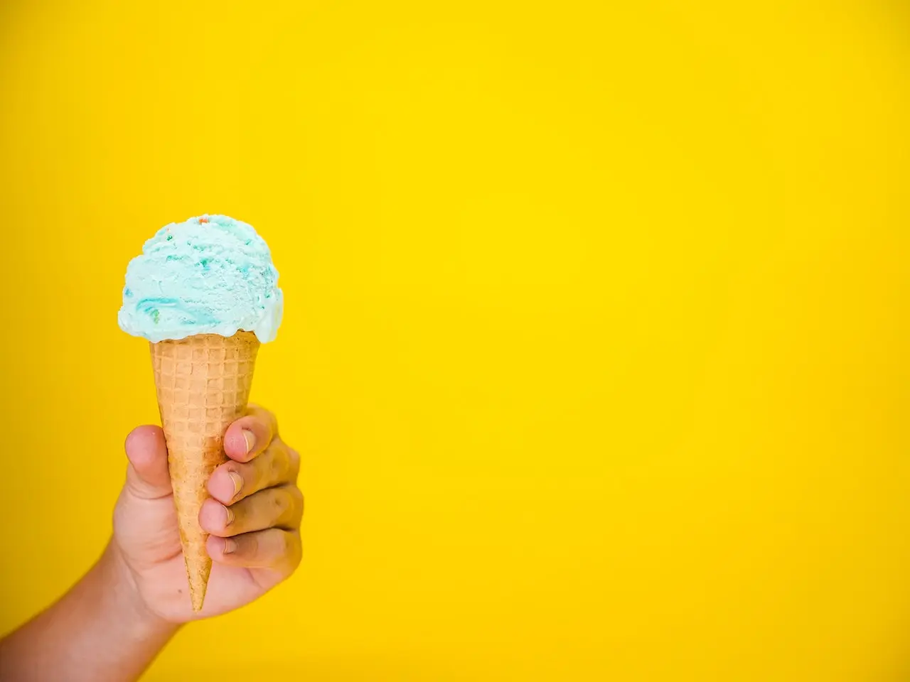 فردی که بستنی میوه ای قیفی در دستش گرفته است و پشت بستنی نیز دیوار زرد رنگی قرار دارد