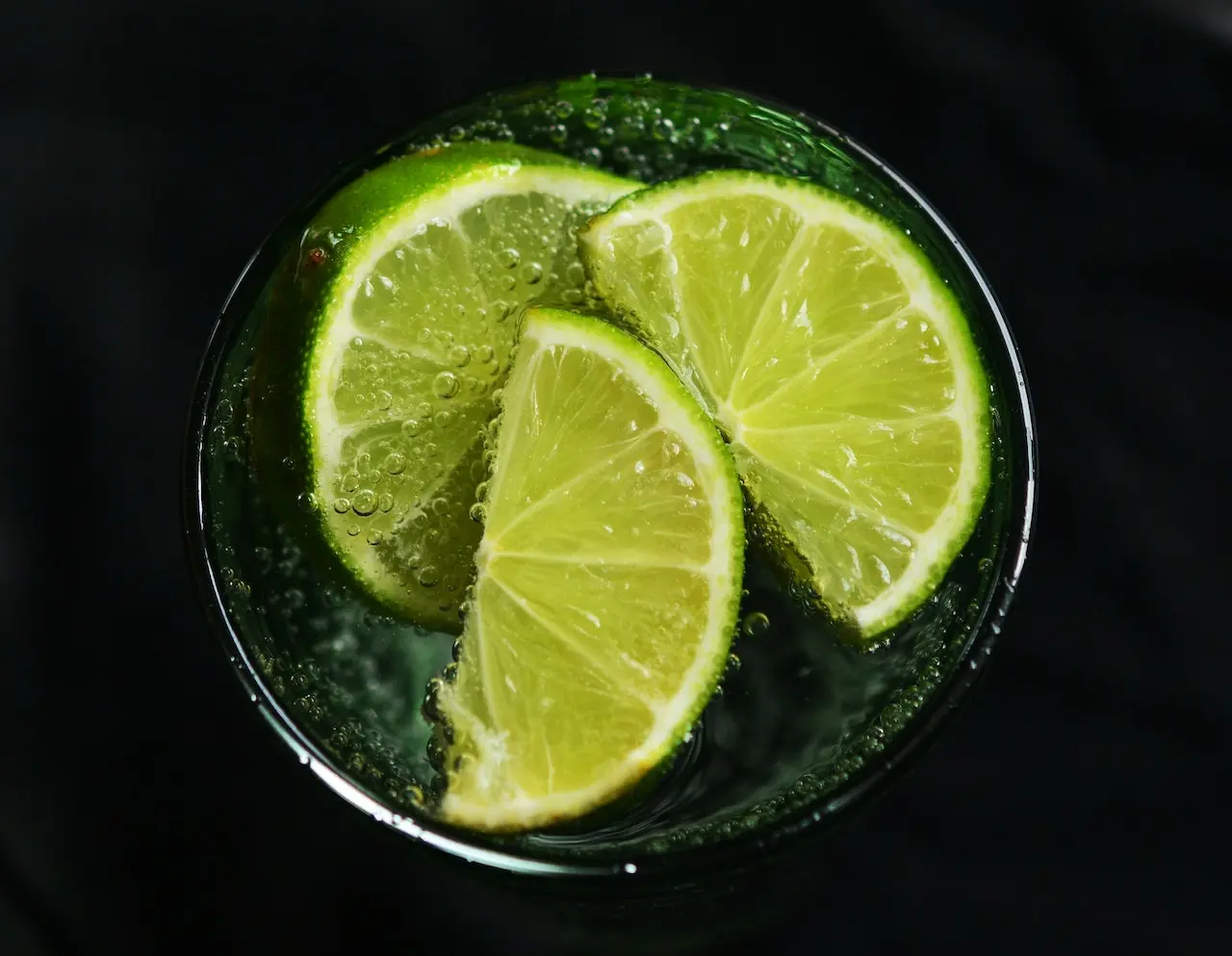 لیمو هایی سبزی که در داخل لیوان مشکی قرار دارد و آب گازدار نیز در آن قرار دارد